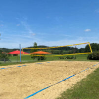 Volleyballfeld mit Sandboden inmitten einer grünen Wiese